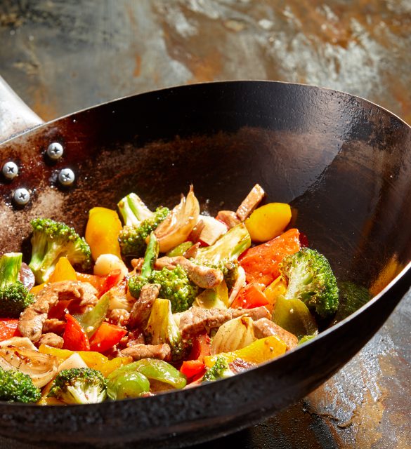 Tasty vegetable dish with broccoli and colorful peppers cooked in oil stained asian wok recipe against a rustic background