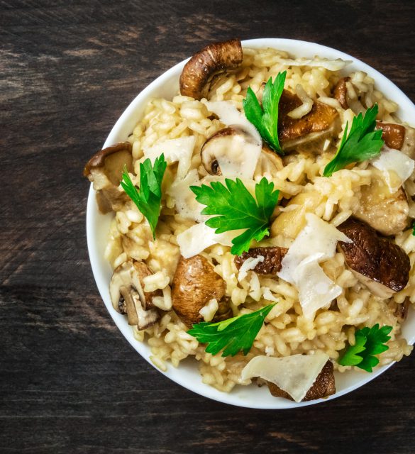 An overhead photo of a mushroom risotto with champignons, fresh parsley, porcini, and Parmesan, on a dark rustic texture with a place for text