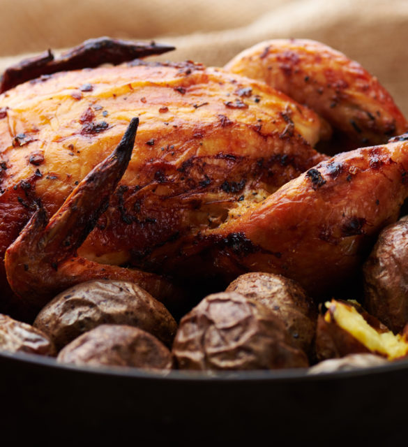 Close view at whole roasted chicken with potatoes on a wooden rustic background